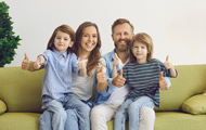Symbolbild niedrige Mieten: Zufriedene Familie mit Kindern auf dem Sofa reckt die Daumen empor 