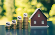 Symbolbild Wohneigentum: Häuschen und Treppe aus Geldmünzen mit Prozent-Zahl-Würfeln als Symbol für steigende Preise und Zinsen