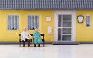 Symbolbild Teilverkauf: Figuren, die ältere Personen symbolisieren, sitzen vor einem Haus auf der Bank